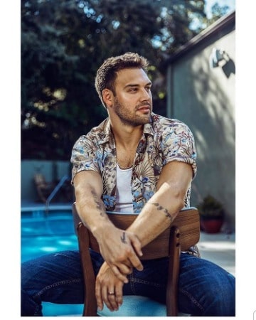 Ryan Guzman in shirt and jeans sitting on chair